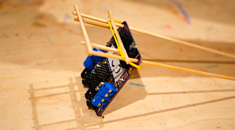 Image of a wooden structure attached to a purple circuit board with a yellow elastic band