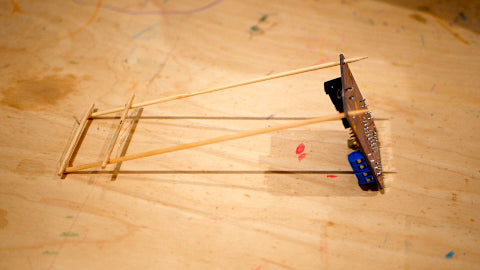 Image of a wooden structure made from pieces of kebab skewers, attached to a purple circuit board