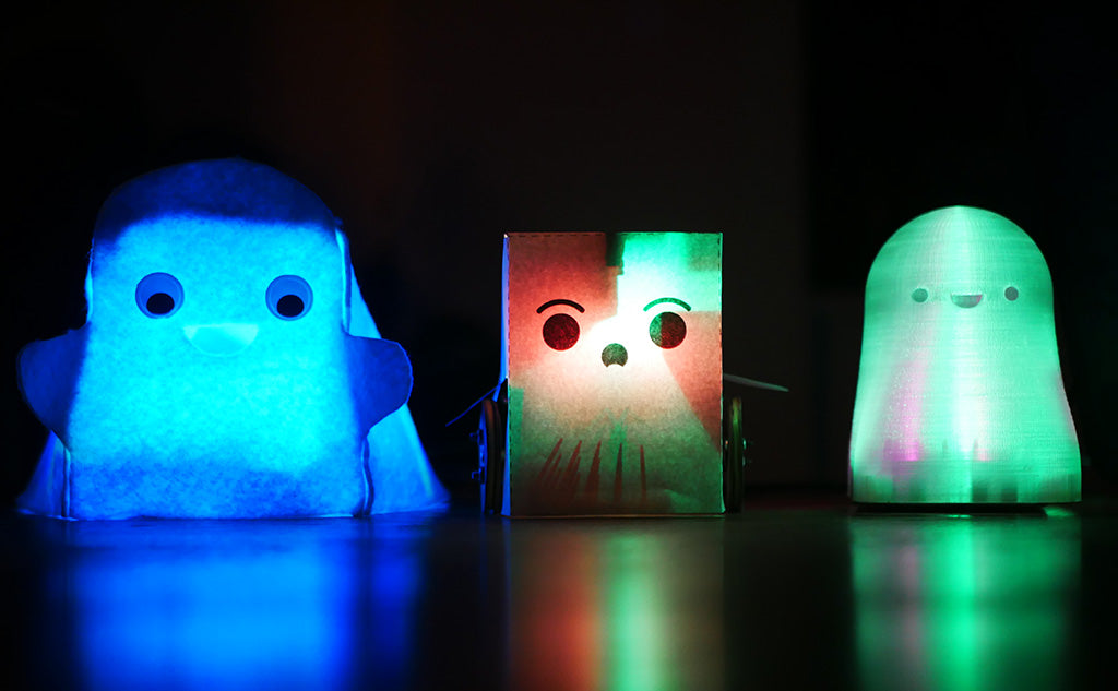 Photo of three small cartoon-style ghosts all internally illuminated with coloured light, one made of felt, one made of paper and one made from frosted plastic