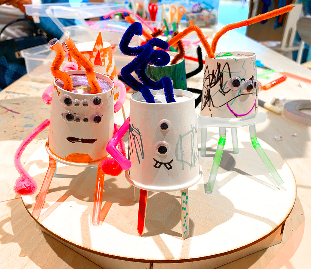 Four paper cup based robots with straws and coffee stirrers for legs, plenty of goggly eyes and marker decoration.