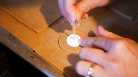 Image of a small white disc placed in the centre of a circled piece of gingerbread dough, and a bamboo skewer poking holes through the white disc into the dough.