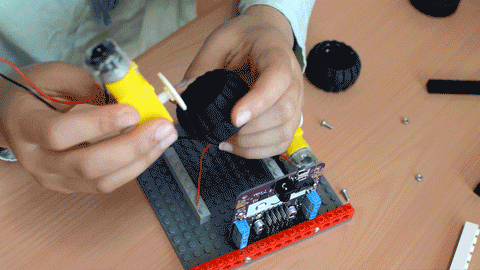 GIF showing a pair of hands pushing a black wheel onto a yellow motor