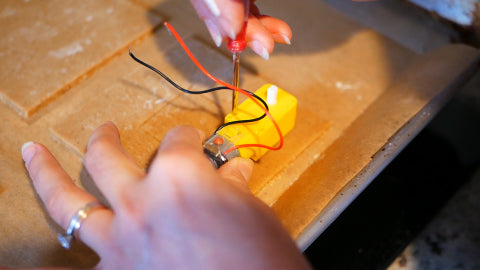 Image of a small yellow motor with gingerbread dough underneath it, and a red screwdriver poking holes through the yellow motor into the dough.