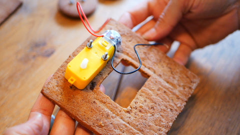 Image of a yellow motor screwed into a gingerbread side wall, that includes a small window.