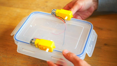 Image of two yellow motors attached to the lid of a Tupperware container.