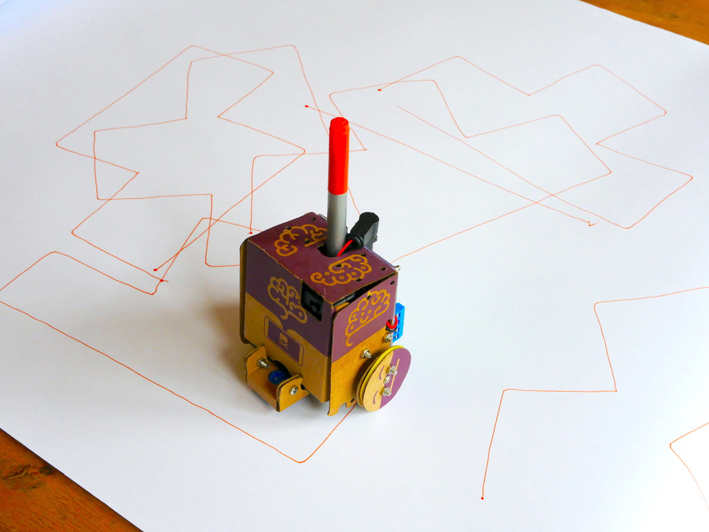 Image of a cardboard robot holding an orange pen, on a roll of white paper