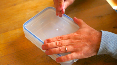 Image of someone poking a hole in a Tupperware container using a masonry nail.