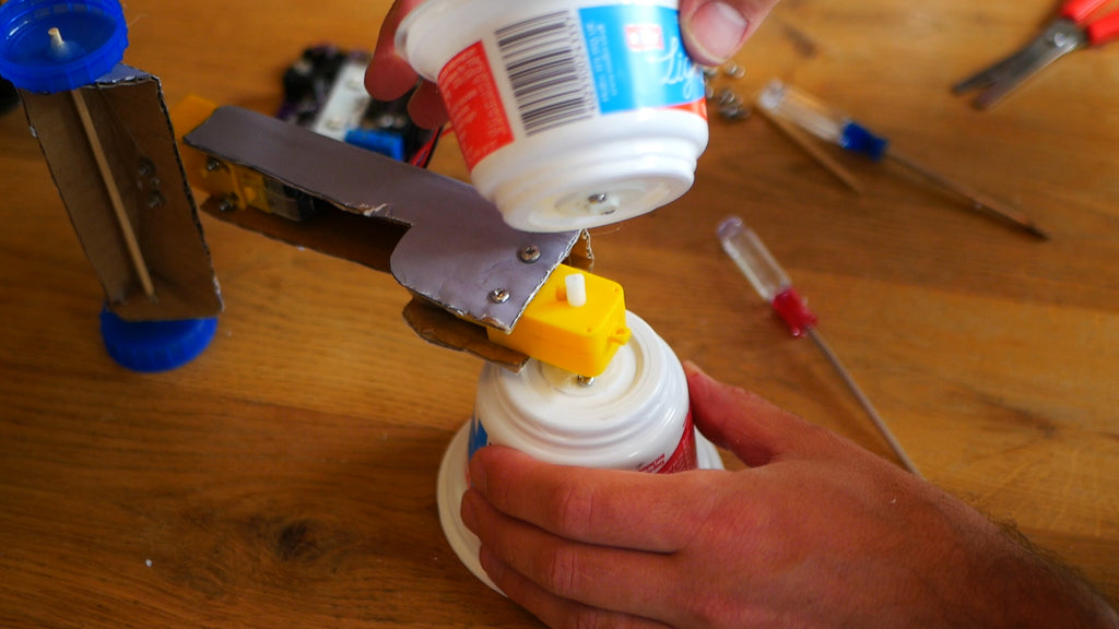 Image of a yoghurt pot being attached to a yellow motor that acts as an axle.