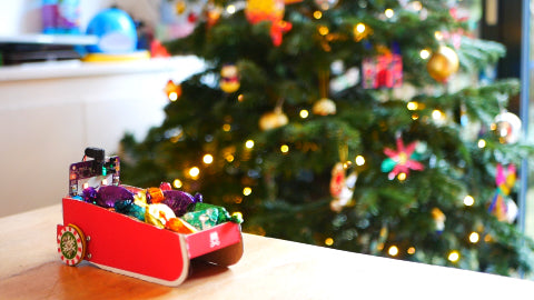 Image of a paper reindeer and a red light-up nose, with a Christmas tree in the background.