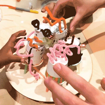 Looping film of five vibrating paper cup robots placed on a circular wooden platform and knocking each other off