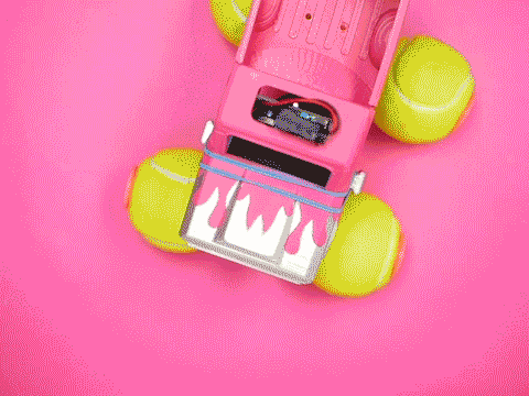 Looping video of a pink toy monster truck with yellow tennis ball wheels driving on a pink background, viewed from above