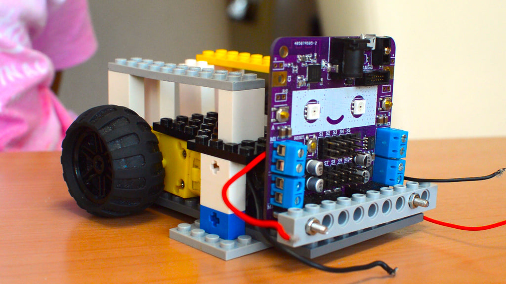 A picture of a half-done robot made out of LEGO bricks and a circuit board with a smiling face