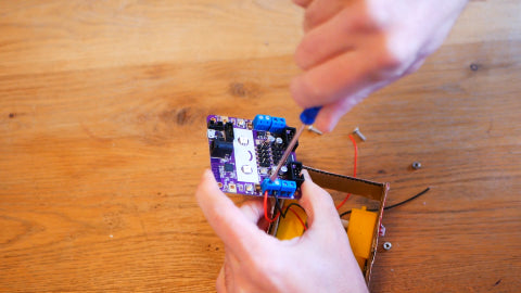 An image of a screwdriver screwing up a small blue chamber on a purple circuit board