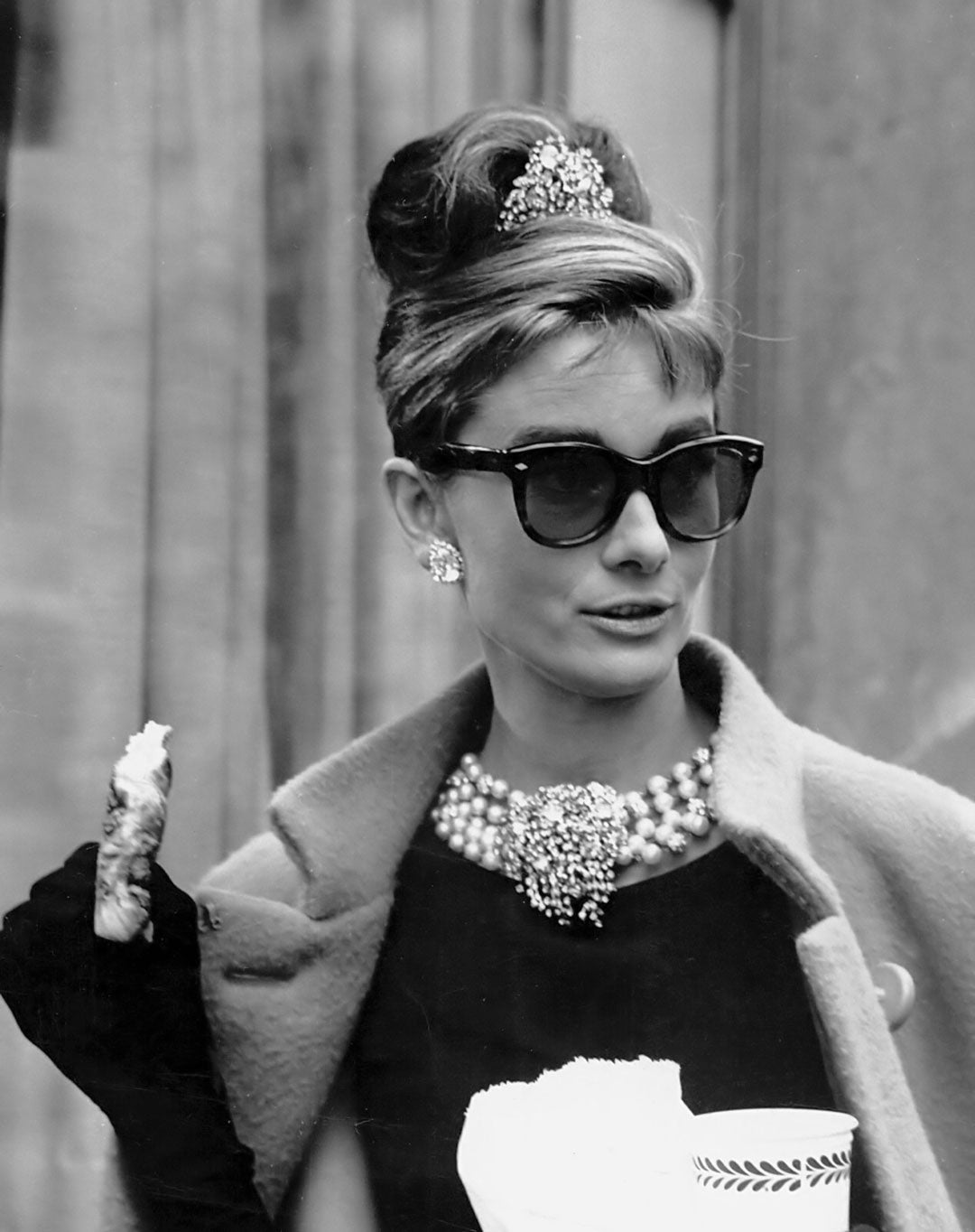 Actress Audrey Hepburn wearing sunglasses and black dress holding coffee cup