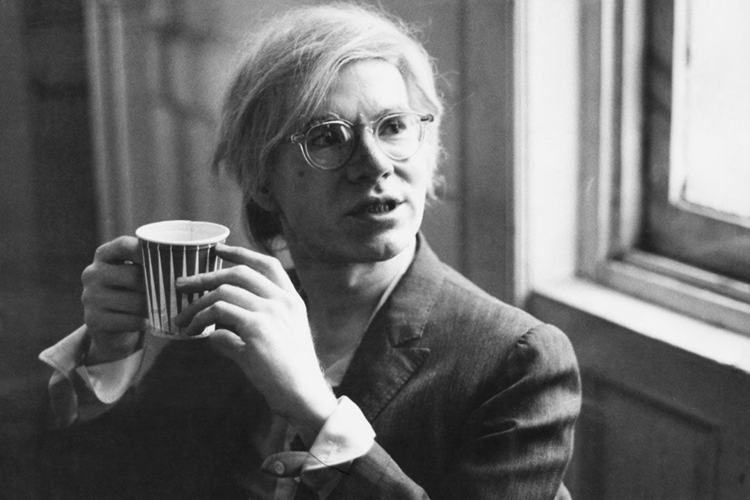 Andy Warhol drinking coffee wearing a suit and clear glasses frame
