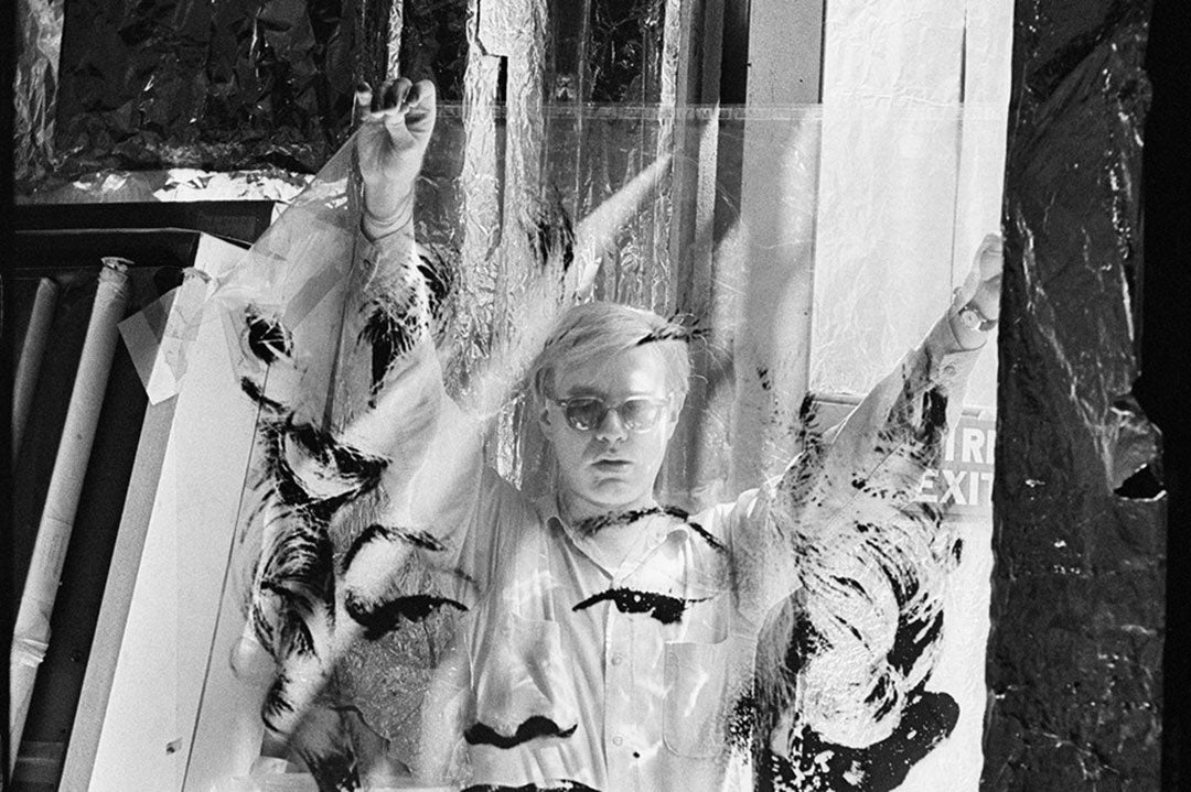 Andy Warhol wearing sunglasses holding screen print of Marilyn Monroe