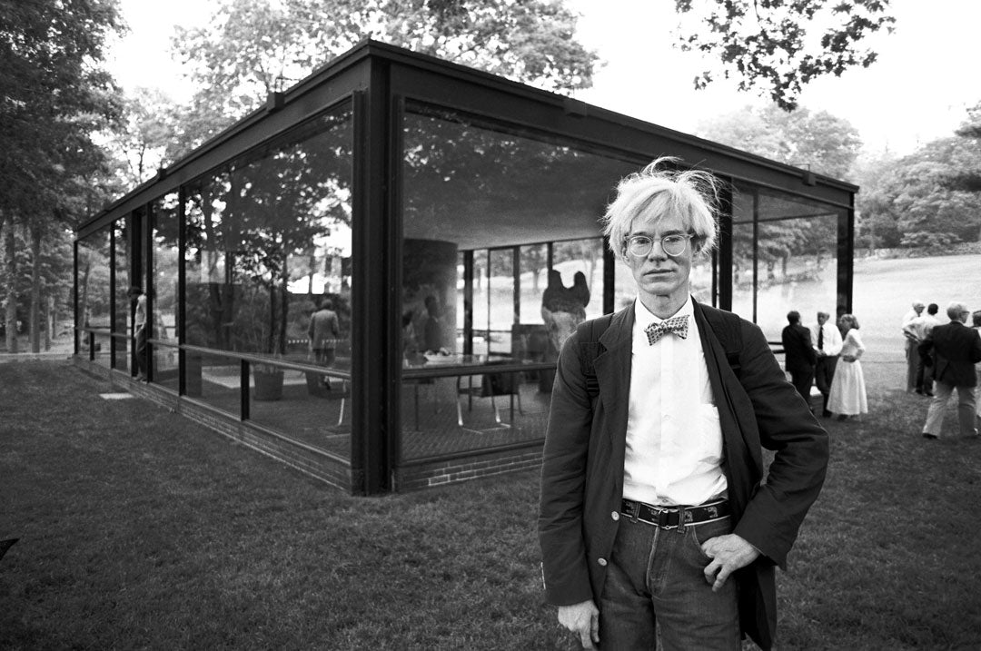 Artist Andy Warhol wearing suit and bow tie outside glass building