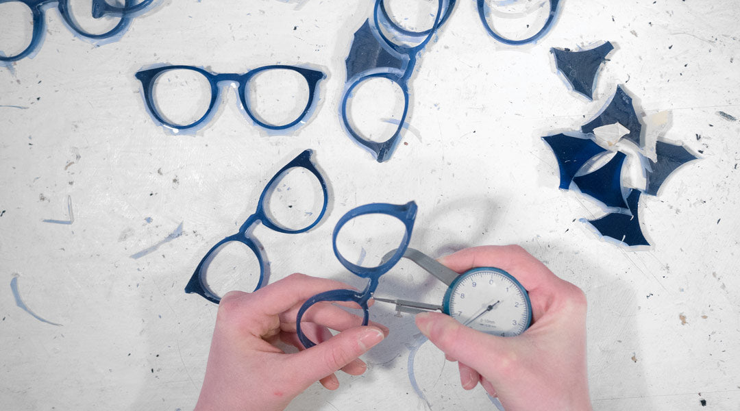 Blue glasses frames being checked for thickness consistency during manufacture