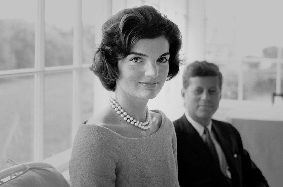 Jackie Kennedy sitting in front of her president husband JFK