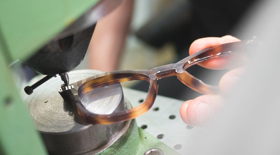 Orange and black sunglasses frame being fitted with hinges using a green machine