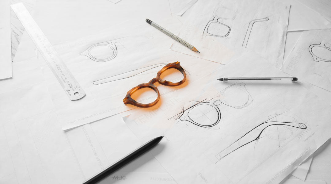 Orange sunglasses frame lying upon sketches of other sunglasses designs