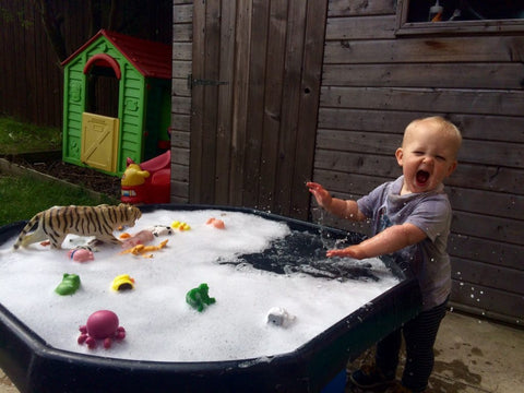 Child outdoors splashing in bubbles with toys