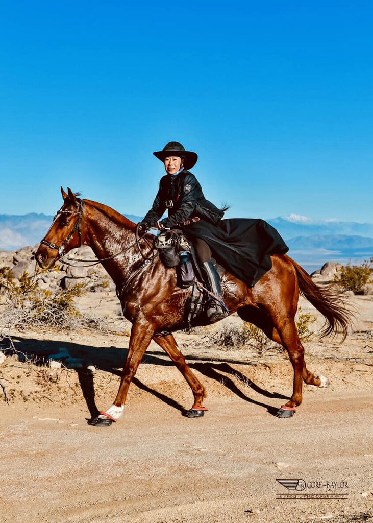 Dawn Champion riding a wet, brown horse wearing red Scoot Boots in the desert