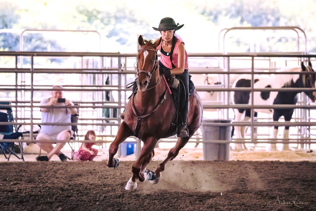 Dawn Champion riding her brown horse wearing blue Scoot Boots on a barrel racing course