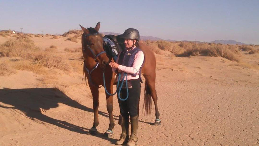 Woman petting her brown horse wearing blue Scoot Boots in the desert