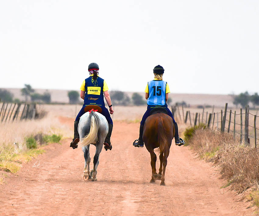 Riders riding down a dirt road in a horse riding competition in Scoot Boots