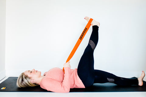 reclined hand to big toe pose with supine twist yoga pose with shoulder strap prop