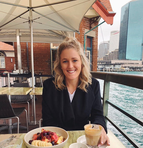 young nutritionist (Jemma McEwan) sitting at table with a bowl of fruit and coffee
