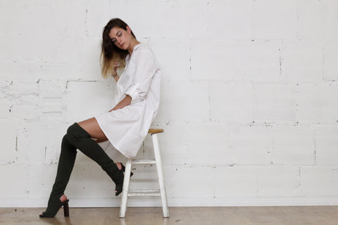 woman sitting on a stool wearing a white shirt and long boots