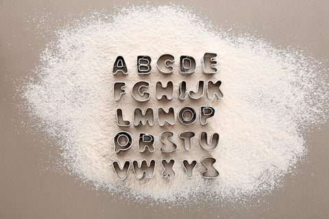 Phonetic Alphabet shaped cookie cutters on scattered flour.