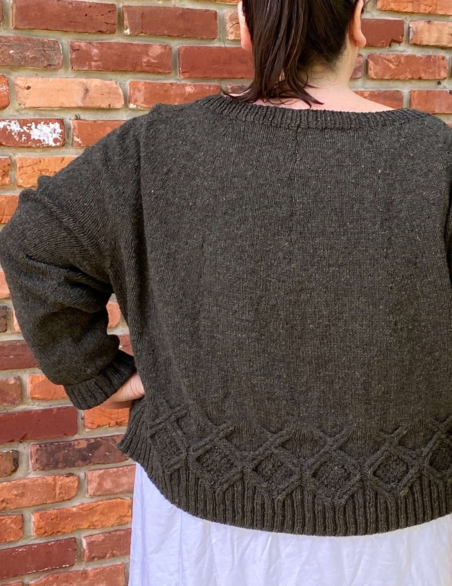 the back of a brown sweater, worn by a model standing in front of a brick wall