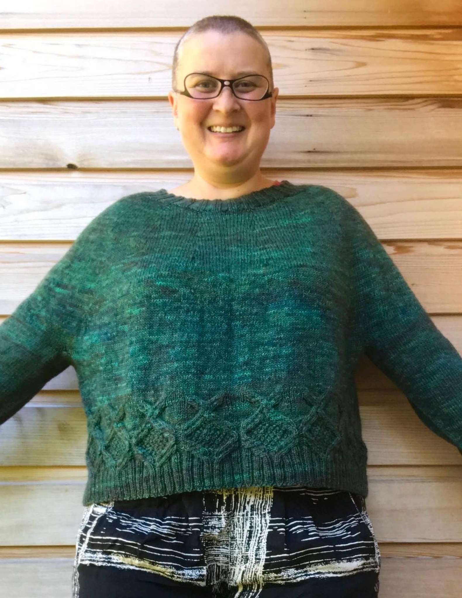 a smiling white, fat, and middle-aged model standing and wearing a green sweater with arms outstretched