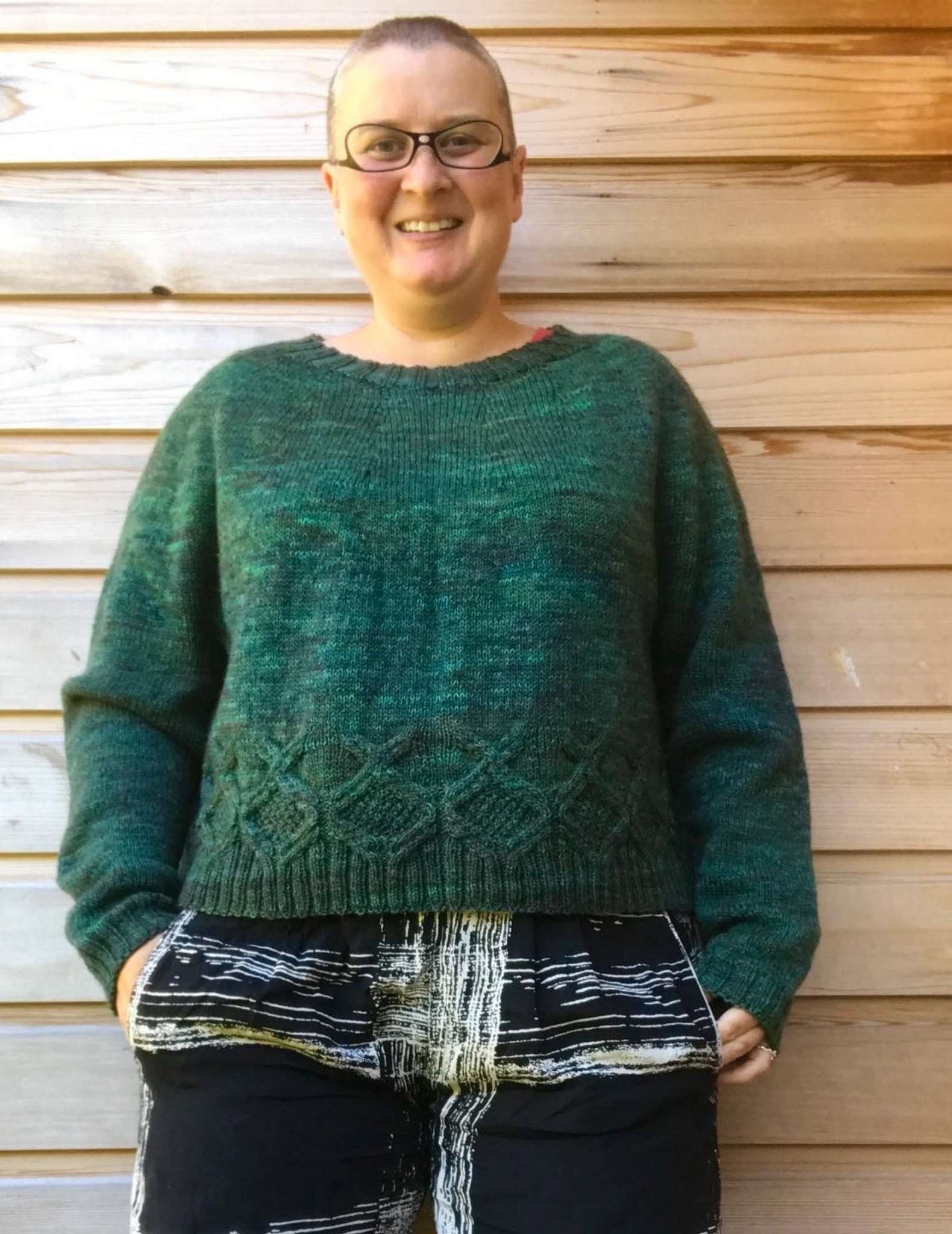 a smiling white, fat, and middle-aged model wearing a green sweater, standing with her hands in her pockets