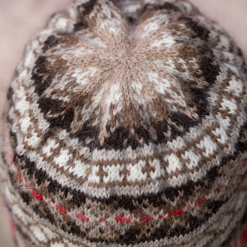 A close-up image of the top of a classic fair isle hat in neutral colours with a red accent stripe