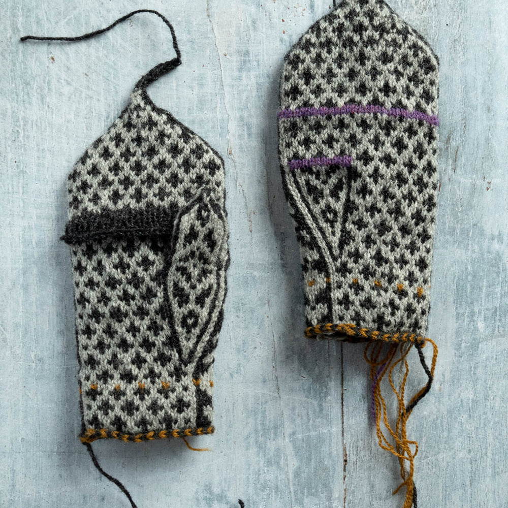 Broughton mittens in grey and black stranded colourwork, laying flat on a grey wood surface