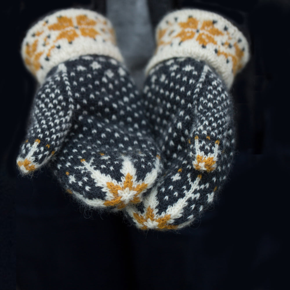 Close up palms of woollen colourwork knit mittens twith white and gold stars at the fingertips and a decorative white with gold star cuff. The main hand of the mitten is navy blue mitten with white flecks.