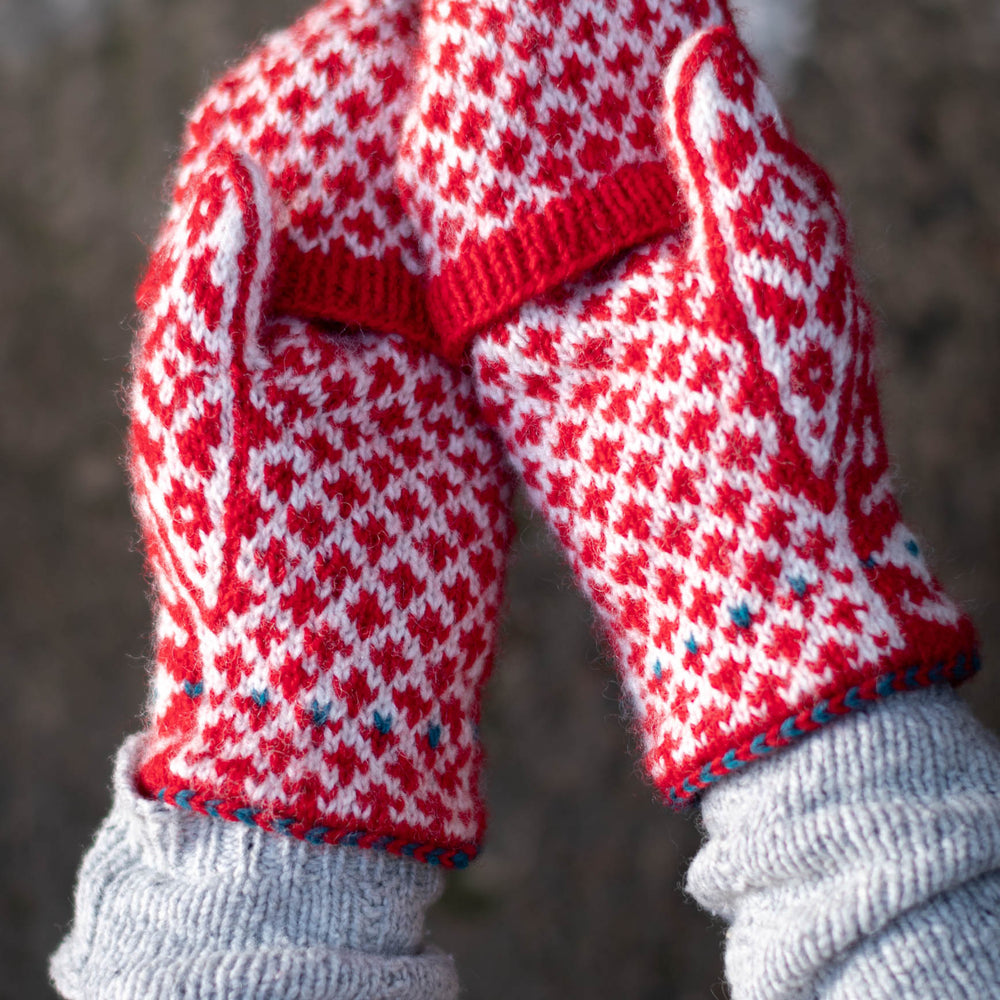two hands, palms facing up, wearing red and white stranded colourwork mittens with a bold red and white diamond motif. the mittens have flip-tops