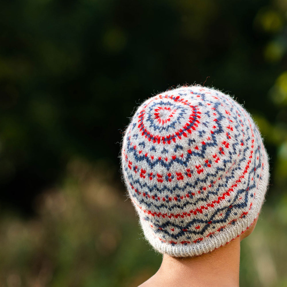 Close up shot of the back and crown view of a fair isle colourwork hat in a neutral base with red and blue motifs.