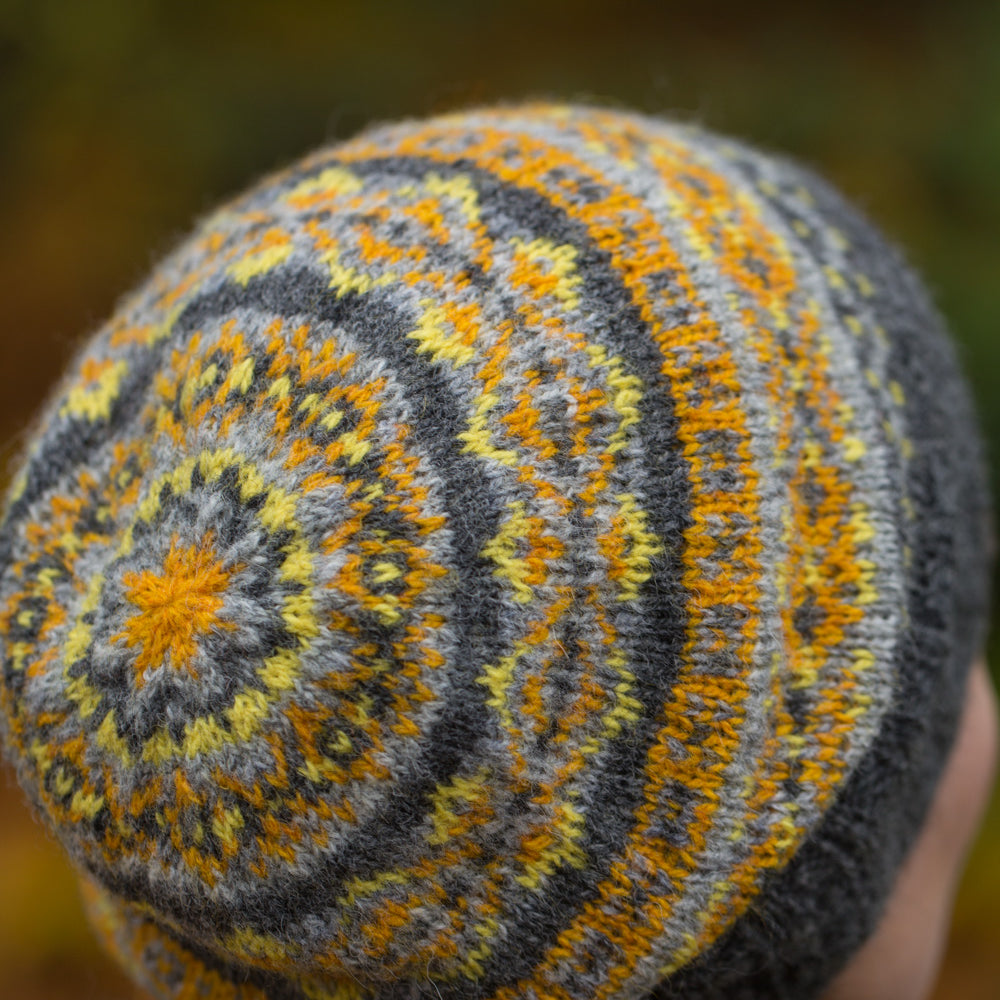 A close-up image of the back of a classic fair isle hat in grey with yellow accents