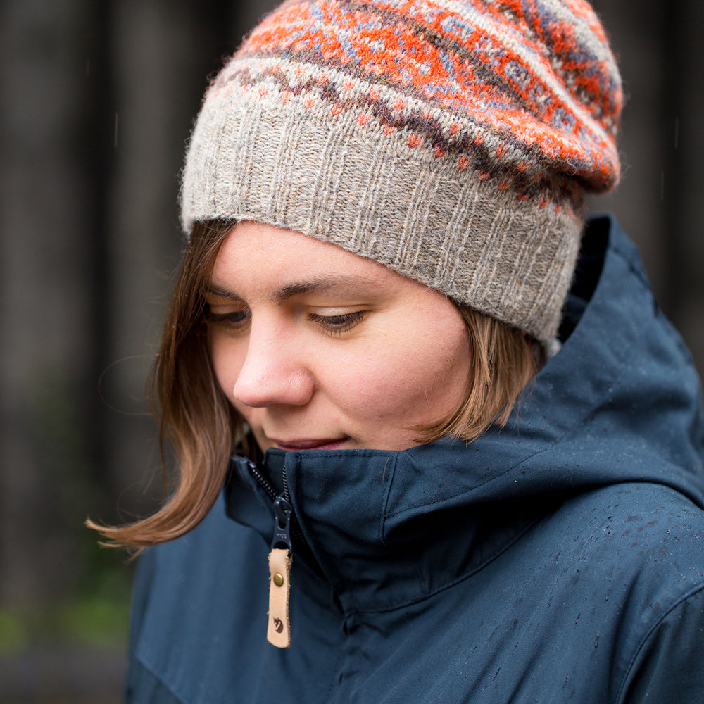 Ysolda, a white woman with chin-length brown hair, is huddled in a blue coat and is looking at the ground. She is wearing an orange and brown fair isle hat.