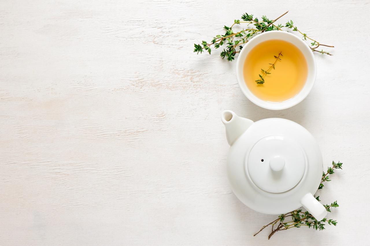 A cup of herbal tea, a teapot and some fresh rosemary