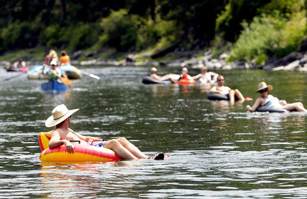 a group of people float in inner tubes down a glassy, slow flowing Clark Fork River near Missoula.