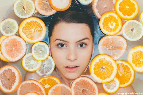 woman face up in bathtub with sliced oranges and a refreshed look on her face
