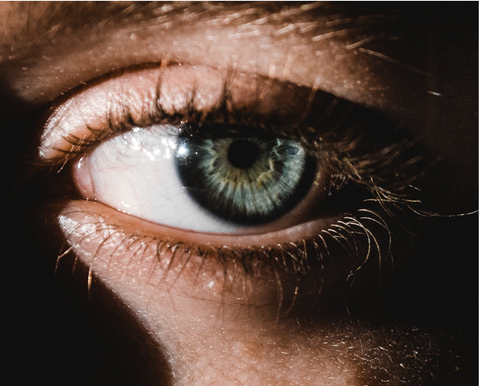 blue human eye in partial light with eyelashes lit and cast shadows