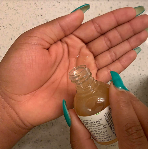 an open palm cupping a clear liquid and the natural skin bleach bottle being tipped by the other hand 