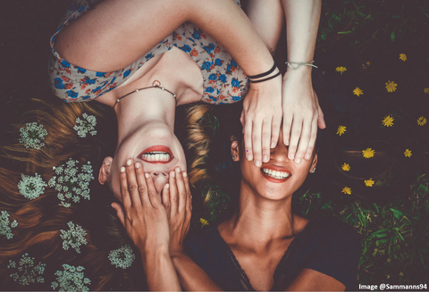 two girls laying down and holding their hands onto each others eyes and smiling
